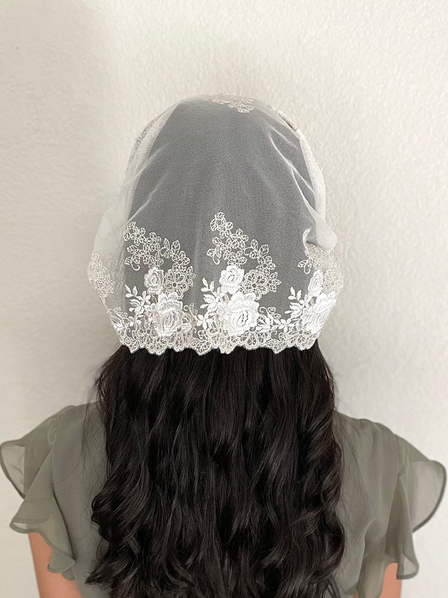 Girl wearing a lace chapel veil with ivory rose embroidery. The small Traditional Catholic Christian Mass mantilla has ties