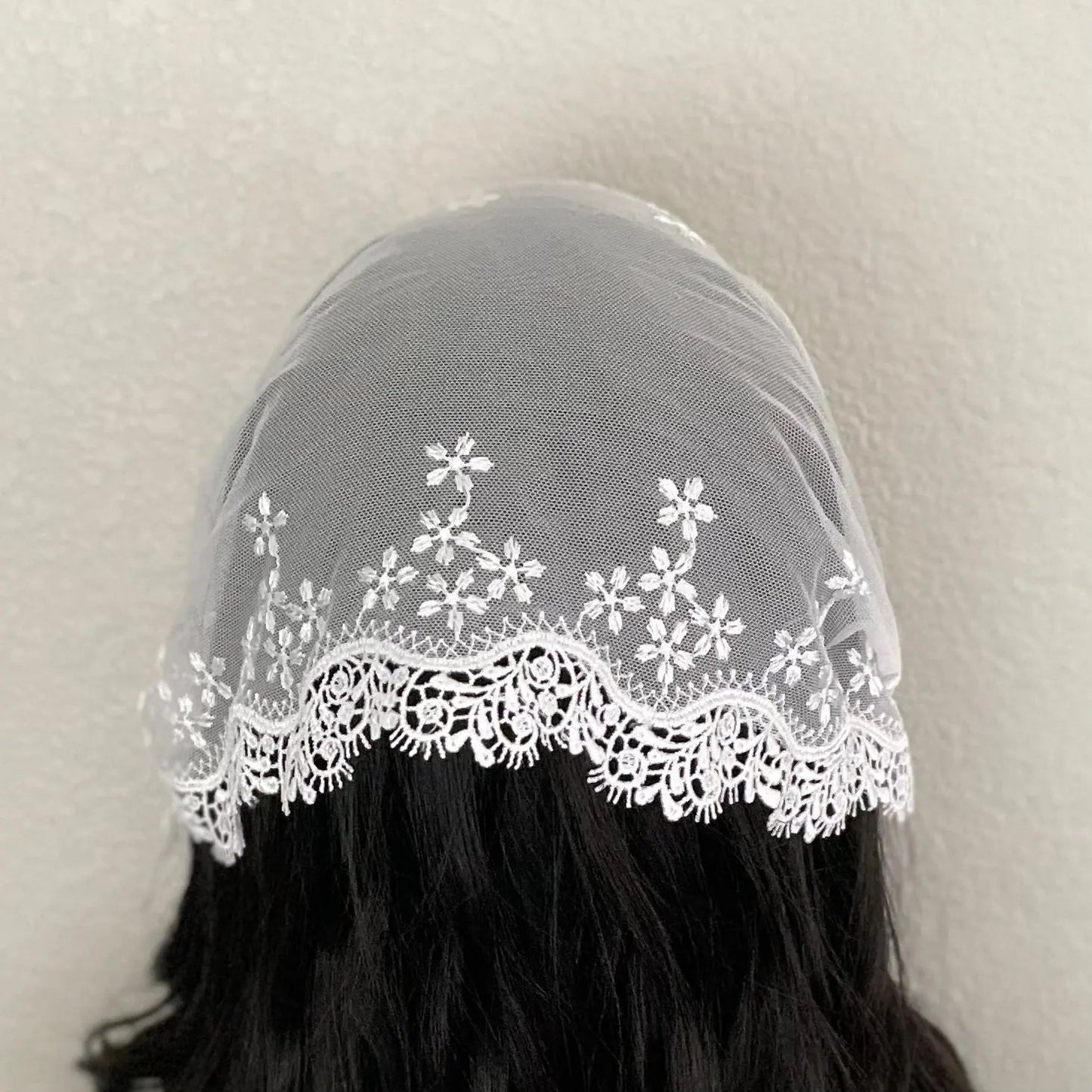 Back view of a girl wearing a one size white lace embroidered Catholic mass chapel veil.
