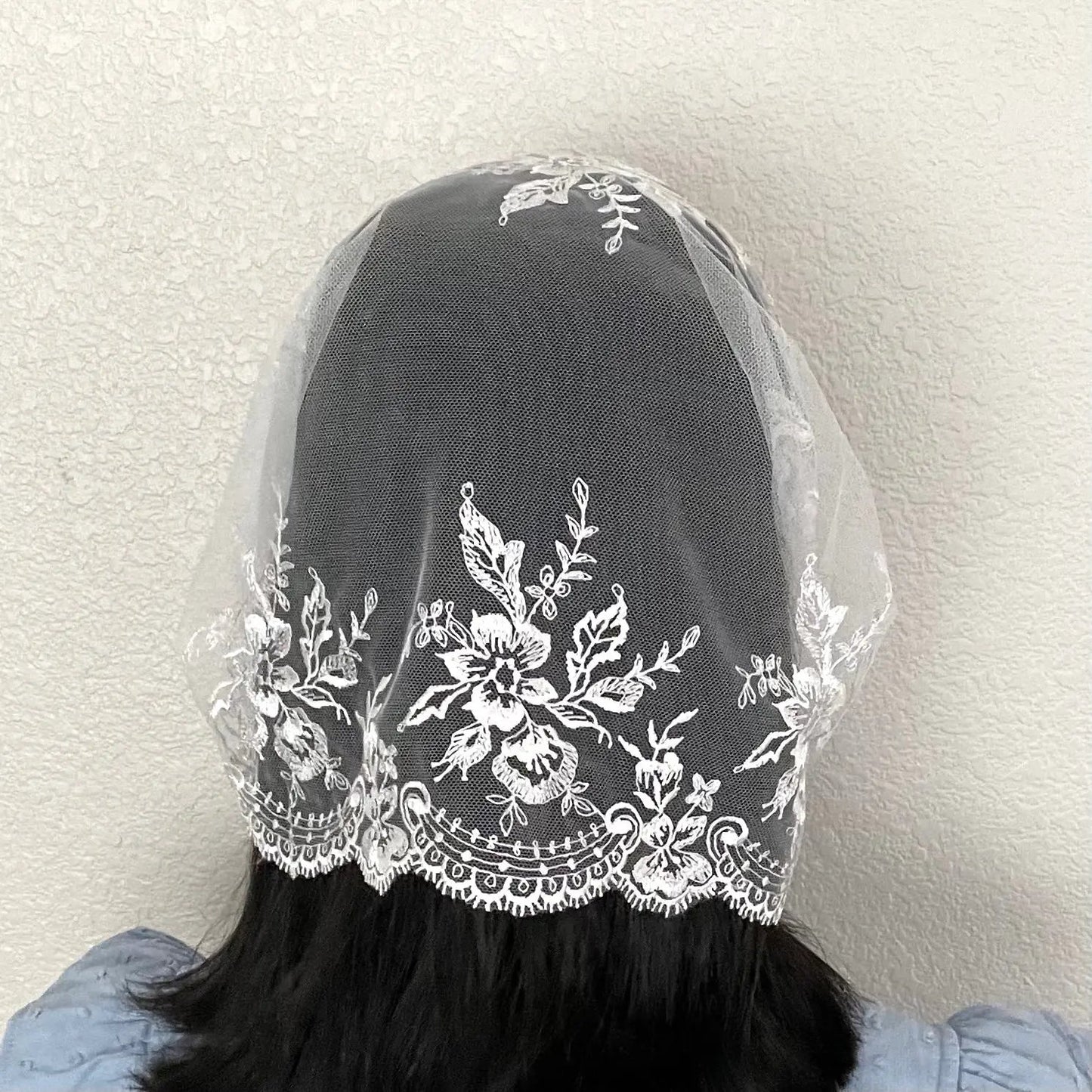 Back view of girl wearing an ivory lace embroidered traditional Christian mass veil headscarf.