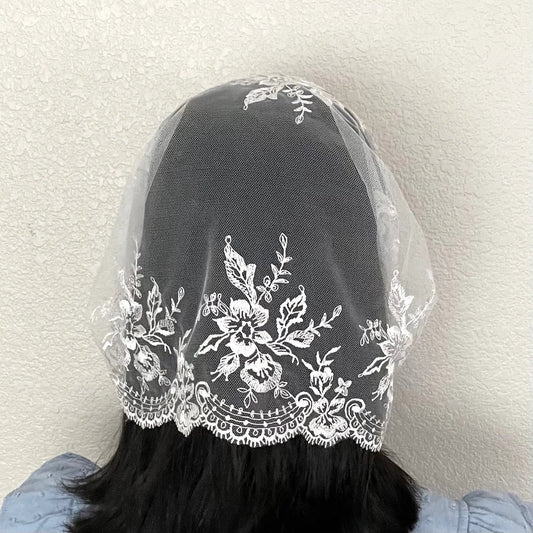 Back view of girl wearing an ivory lace embroidered traditional Christian mass veil headscarf.