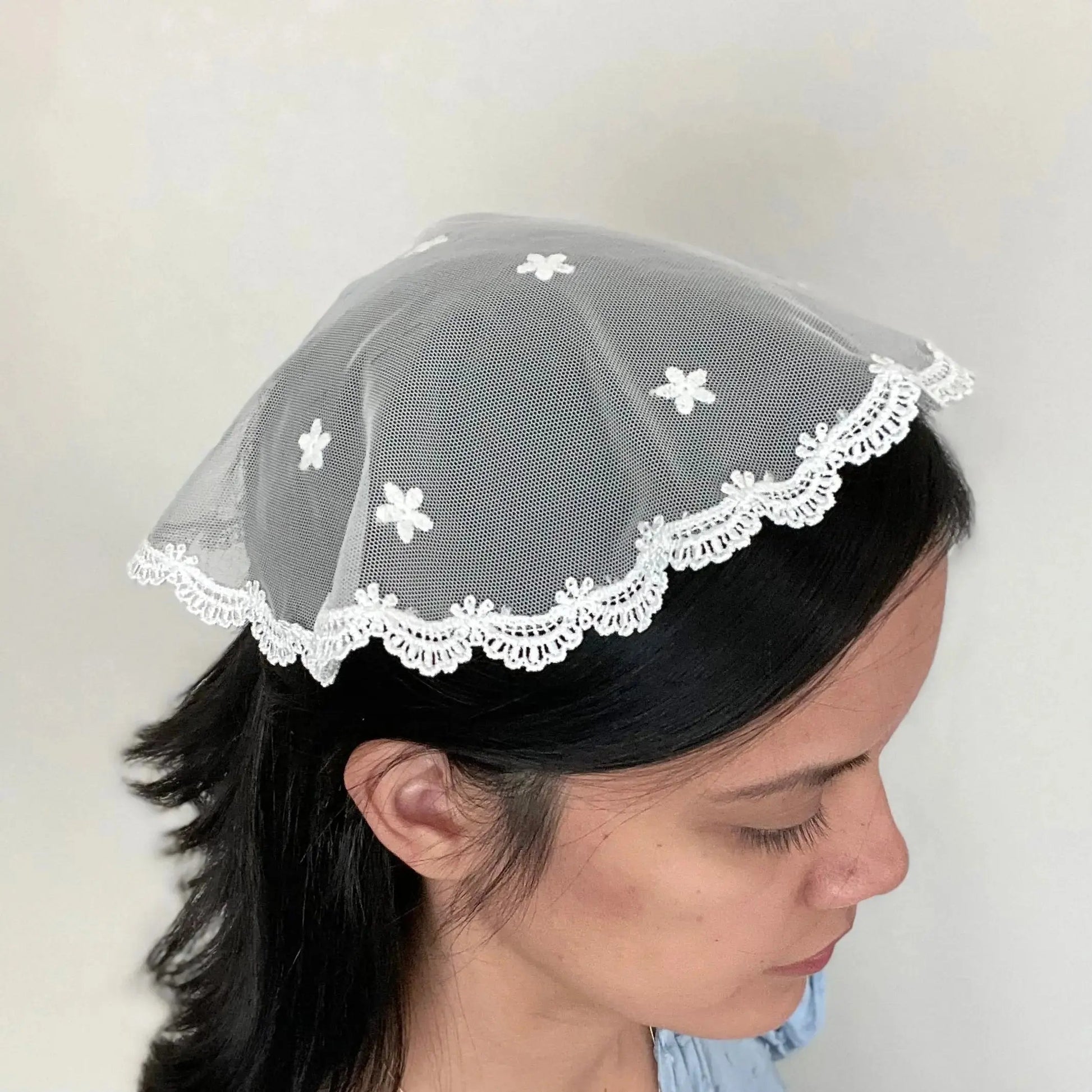 Girl wearing a white embroidered lace cap chapel veil for Traditional Catholic mass.