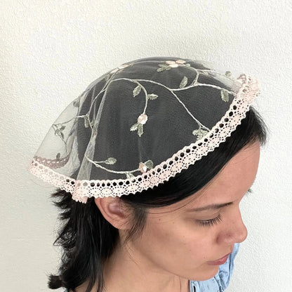 Girl wearing a light pink floral lace cap chapel veil for Catholic mass.
