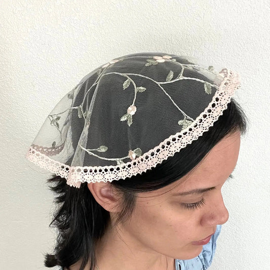 Girl wearing a light pink floral lace cap chapel veil for Catholic mass.
