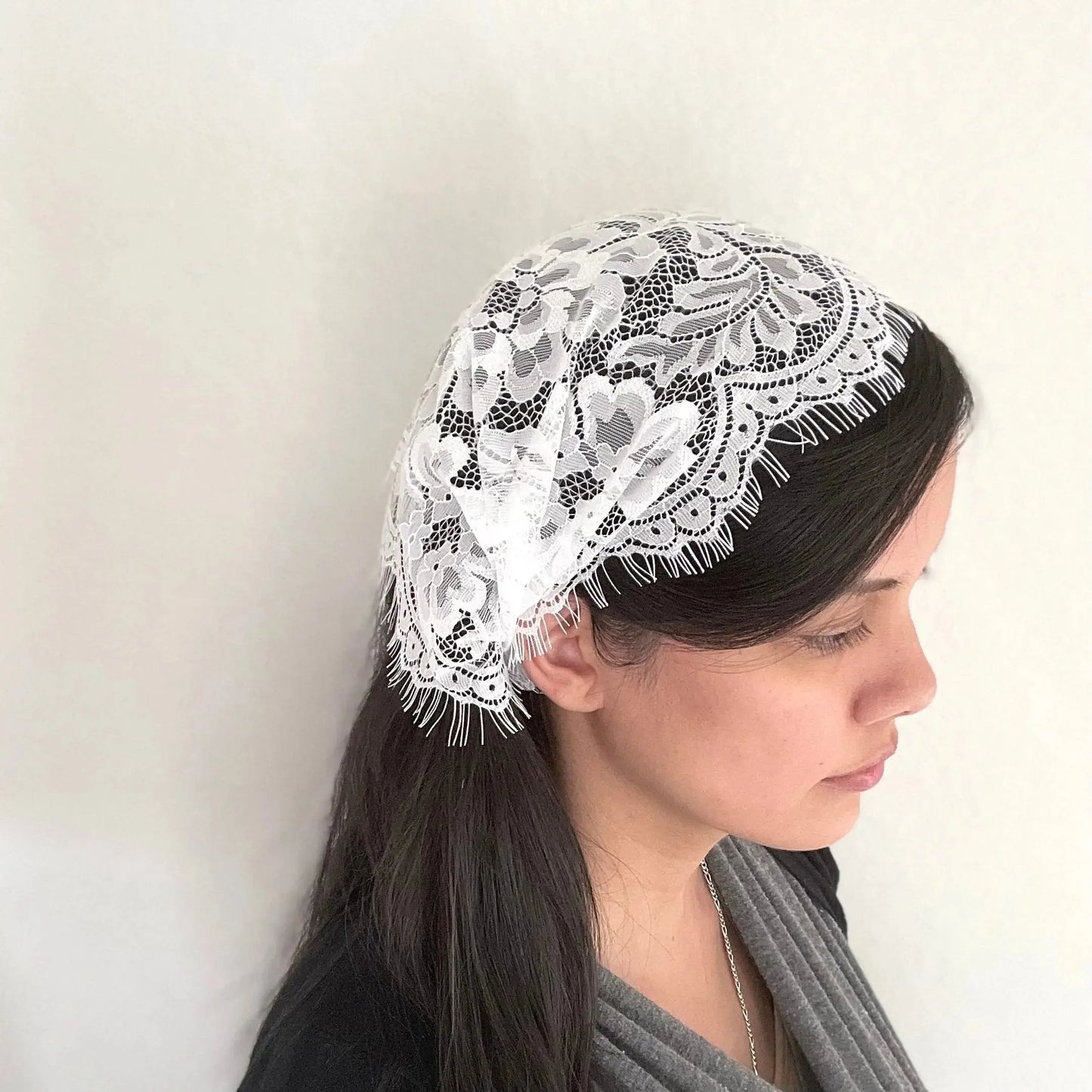 Girl wearing a traditional white eyelash lace chapel veil headwrap for Catholic Mass.
