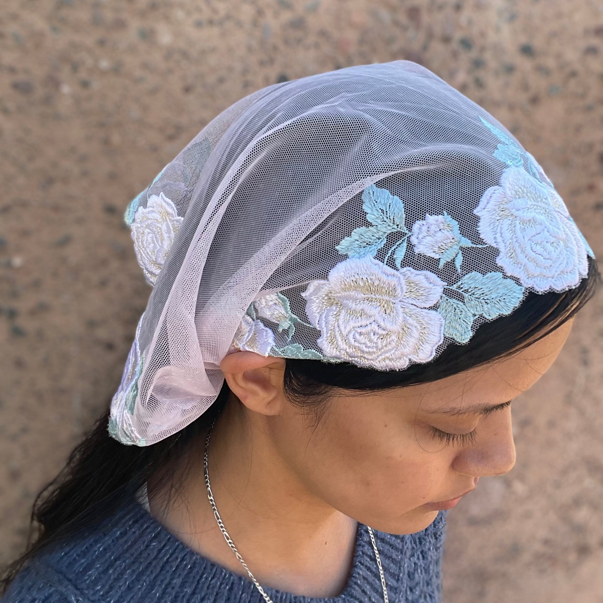 Girl wearing a lace chapel veil with white rose embroidery. The small Traditional Catholic Christian Mass mantilla has ties