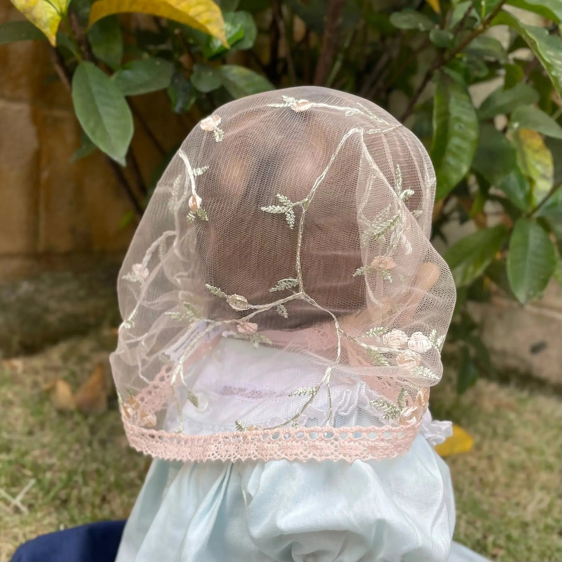 Baby wearing little pink lace veil with floral embroidery. The mantilla is perfect for Traditional Catholic Christian Mass