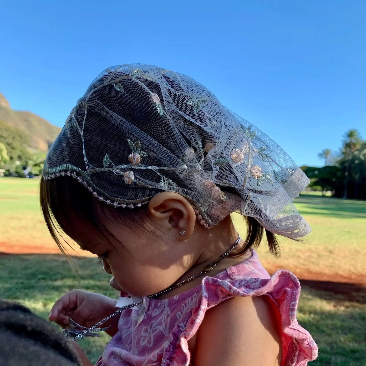 Toddler wearing pale pink lace veil with floral embroidery. The mantilla is perfect for Traditional Catholic Christian Mass