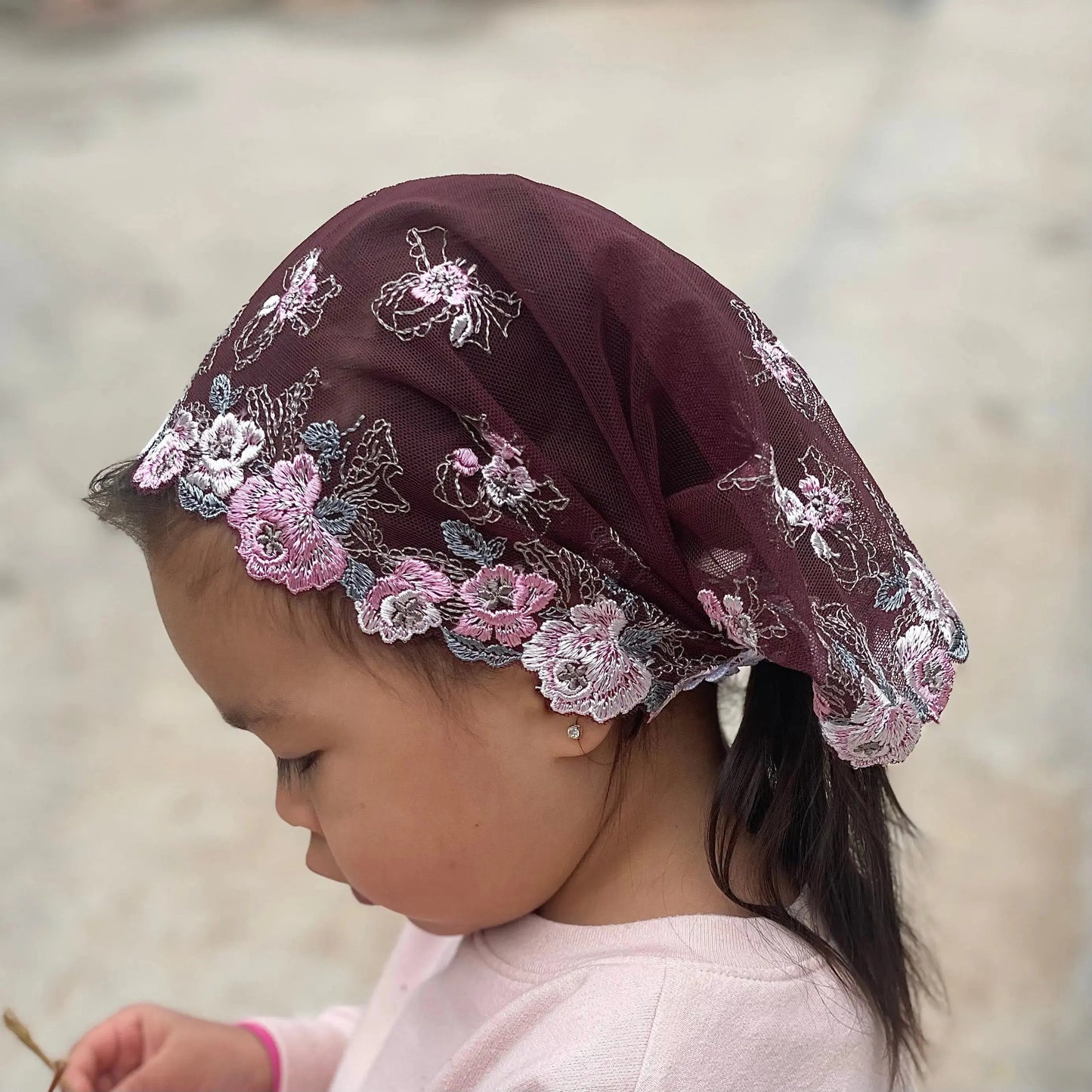 Infant wearing a traditional chapel veil of intricate burgundy lace embroidery for the Lenten season.
