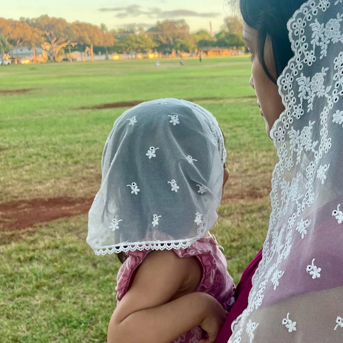 Infant wearing an ivory embroidered lace chapel veil for Catholic baptism.