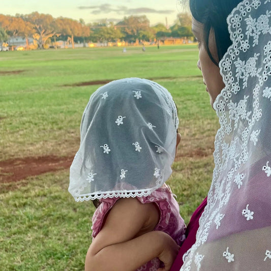 Infant wearing an ivory embroidered lace chapel veil for Catholic baptism.