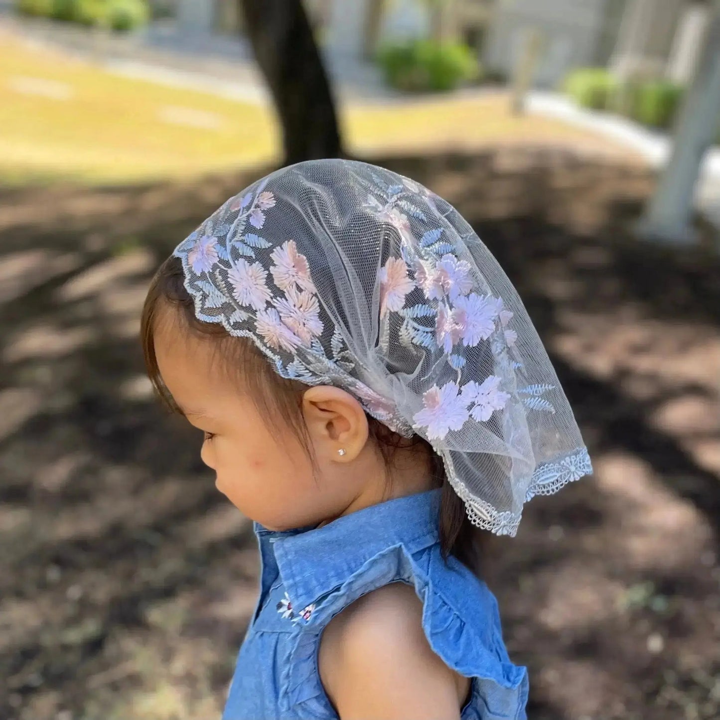 Toddler wearing a traditional Christian chapel veil with pink and grey embroidered lace.