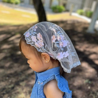 Toddler wearing a traditional Christian chapel veil with pink and grey embroidered lace.