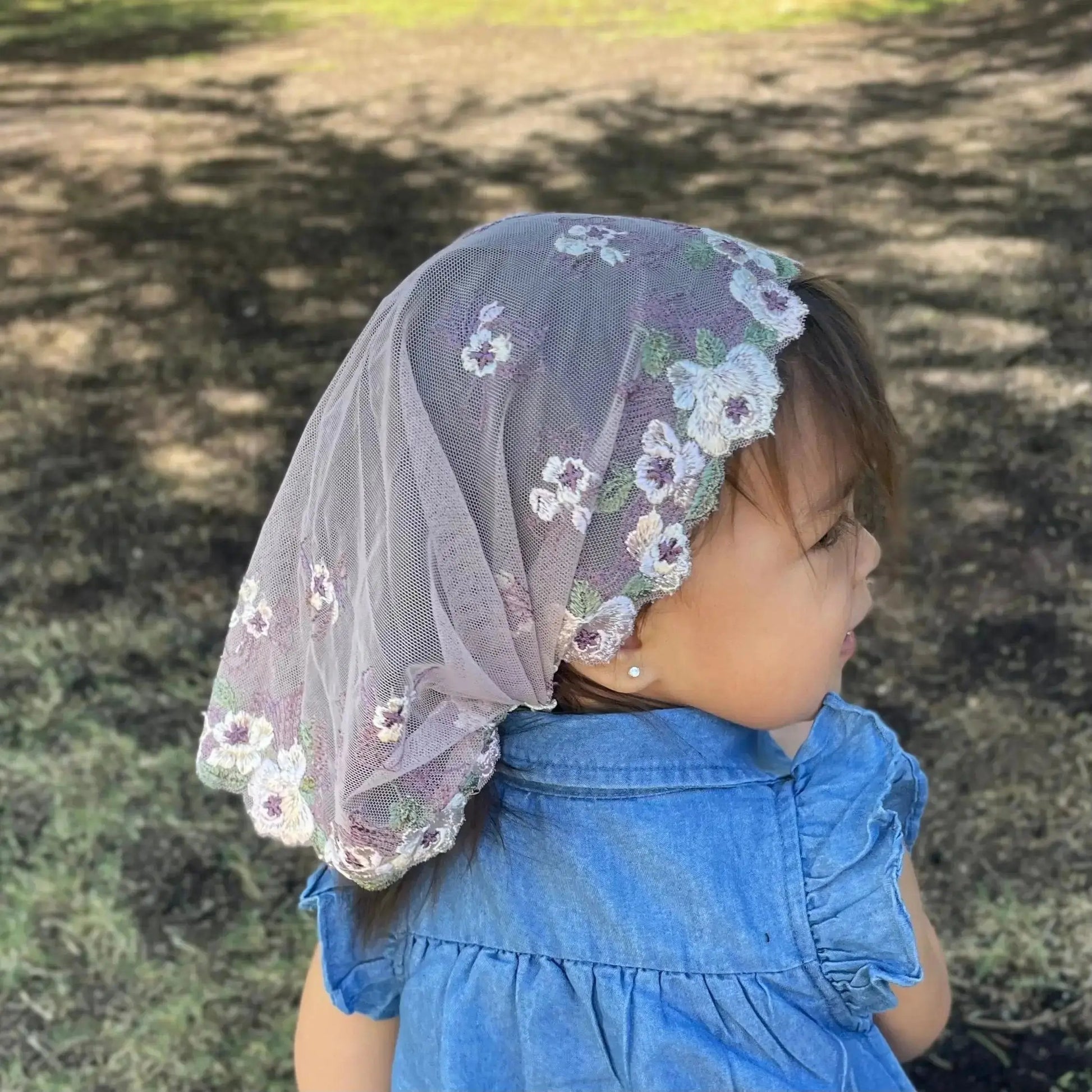 Infant wearing a traditional chapel veil of intricate purple lace embroidery for Catholic season of Lent.