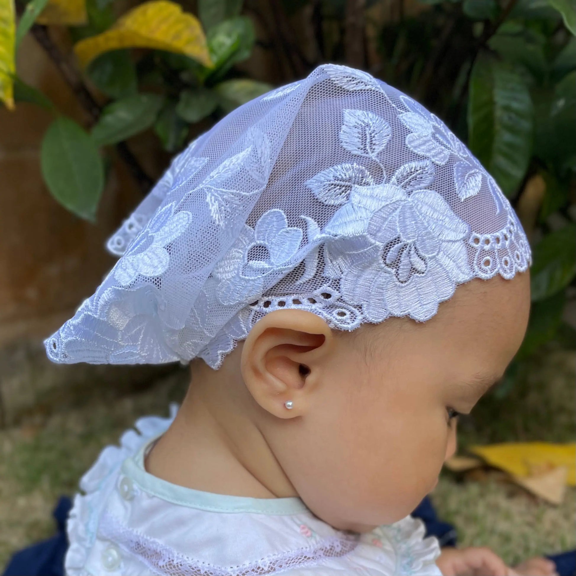 Infant wearing a traditional chapel veil of intricate ivory lace embroidery for Christian baptism