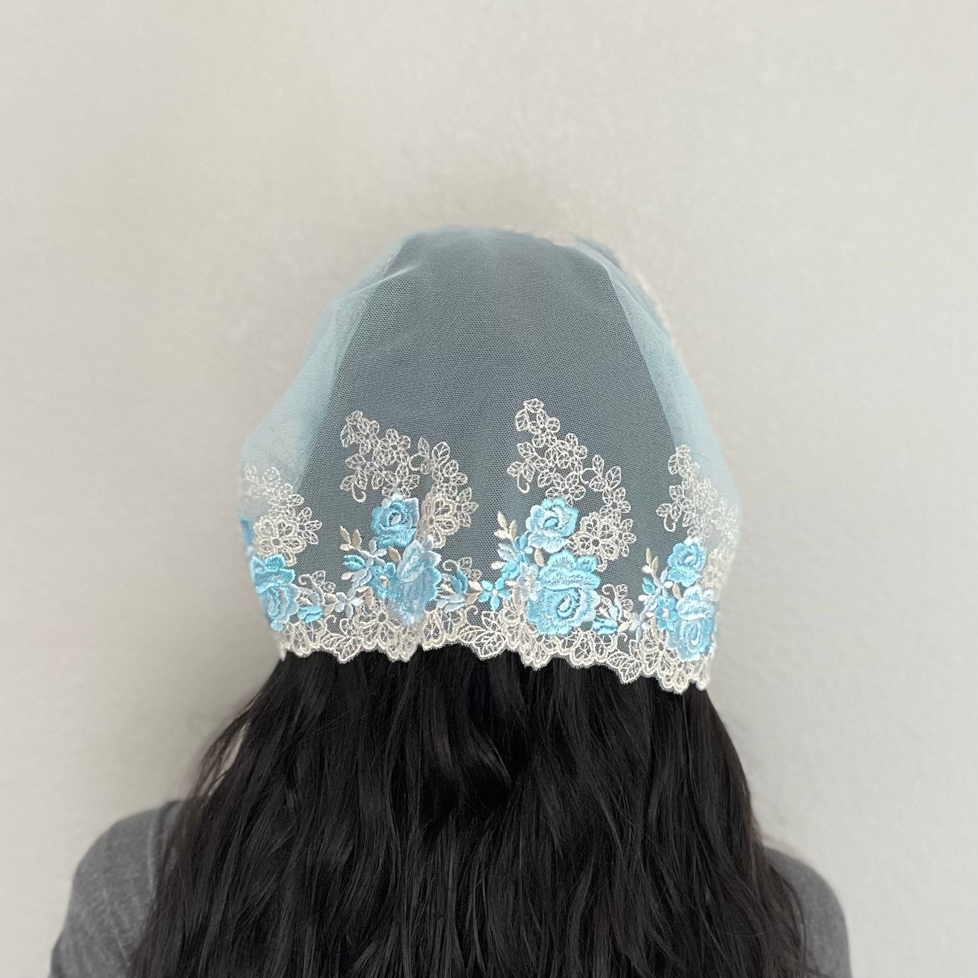 Girl wearing a light blue lace chapel veil with rose embroidery. The Traditional Catholic Christian Mass mantilla has ties