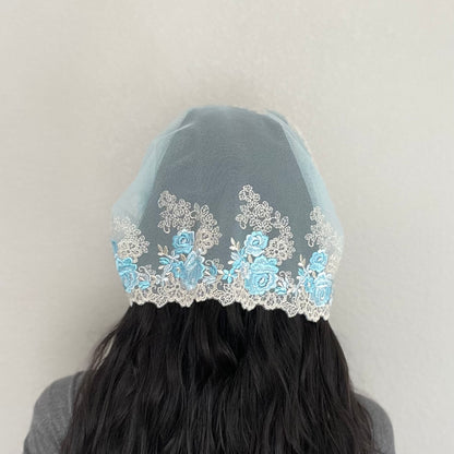 Girl wearing a light blue lace chapel veil with rose embroidery. The Traditional Catholic Christian Mass mantilla has ties