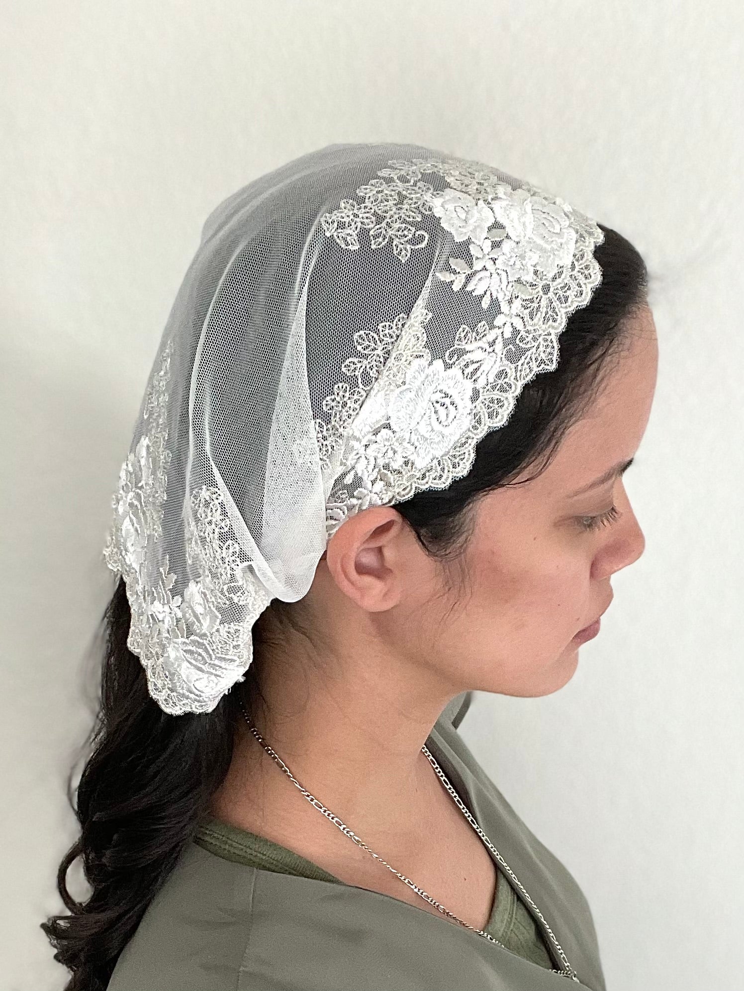Girl wearing an ivory lace chapel veil with rose embroidery. The small Traditional Catholic Christian Mass mantilla has ties